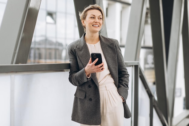 Retrato de uma bela empresária madura de terno e jaqueta cinza sorrindo e falando ao telefone no meio urbano moderno