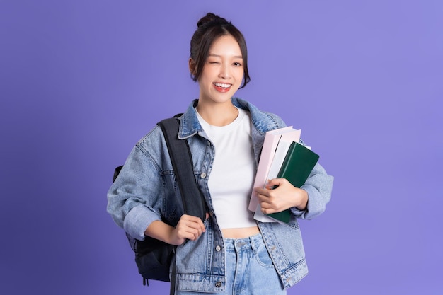 Foto retrato de uma bela estudante asiática usando uma mochila em um fundo roxo