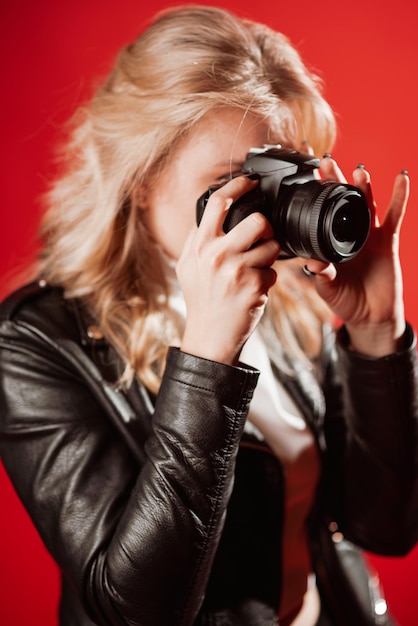 Retrato de uma bela fotógrafa com uma câmera nas mãos que está sendo fotografada em um estúdio fotográfico em um fundo vermelho