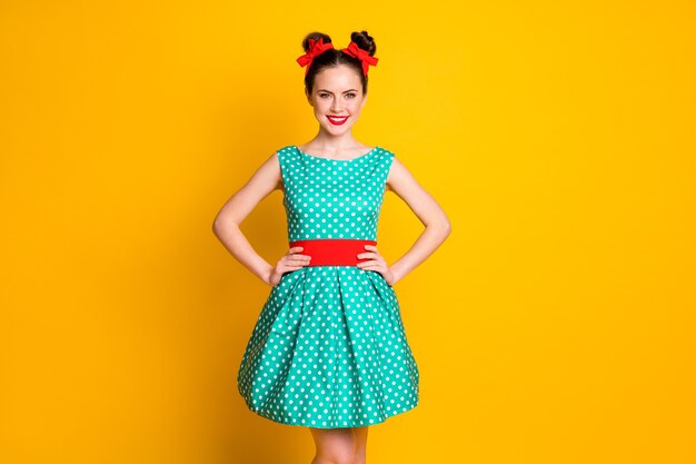 Retrato de uma bela garota encantadora alegre elegante usando um vestido pontilhado com as mãos nos quadris isoladas sobre um fundo de cor amarela vívida