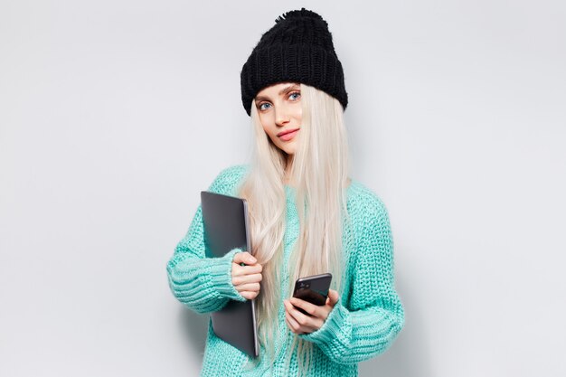 Retrato de uma bela garota loira segurando um smartphone e um laptop