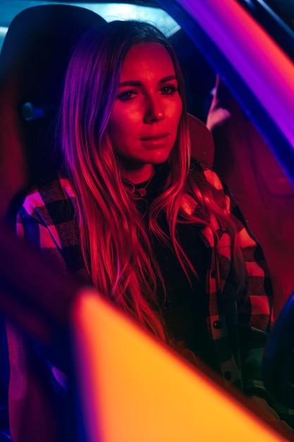 Retrato de uma bela jovem a conduzir um carro à noite à luz de néon