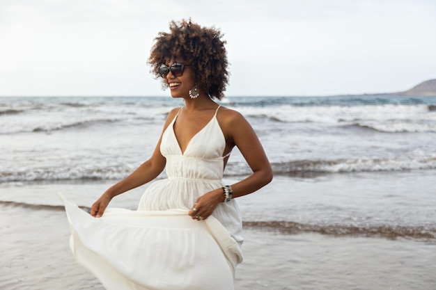 Retrato de uma bela jovem africana sorrindo alegremente com vestido branco e fundo de praia