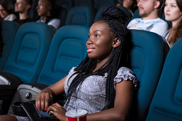 Retrato de uma bela jovem africana sorrindo olhando atentamente a tela enquanto desfruta de assistir a um filme no cinema local