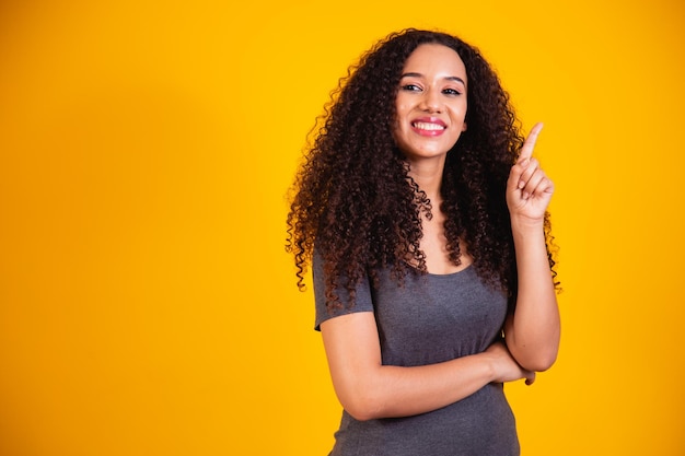 Retrato de uma bela jovem afro-americana com cabelos cacheados, pensando e tendo uma ideia sobre fundo amarelo com espaço para texto. conceito de mulher de boa ideia