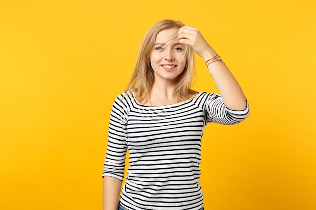 Retrato de uma bela jovem alegre em roupas listradas, segurando o cabelo olhando a câmera isolada em fundo amarelo laranja no estúdio. emoções sinceras de pessoas, conceito de estilo de vida. mock up espaço de cópia.