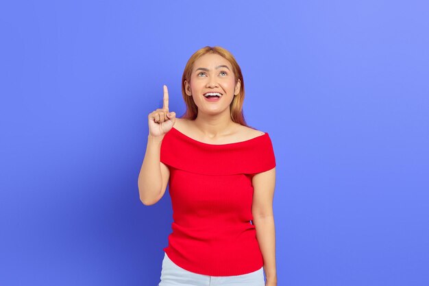 Retrato de uma bela jovem asiática animada apontando para a sala de cópia isolada em fundo roxo