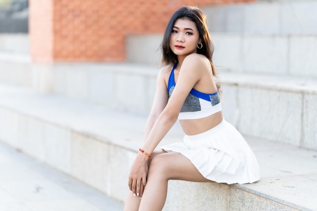 Retrato de uma bela jovem asiática atlética em roupas esportivas da moda em pé e descansando após treinamento de exercício forte no jardim o conceito esportivo ao ar livre do parque