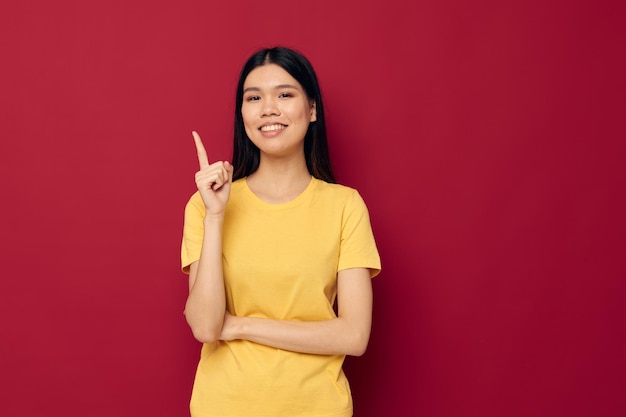 Retrato de uma bela jovem asiática em uma camiseta amarela gesticulando com as mãos divertidas fundo isolado inalterado