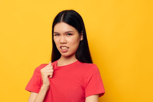 Retrato de uma bela jovem asiática em uma camiseta vermelha posando emoções divertidas fundo amarelo inalterado