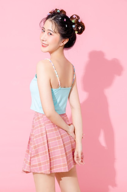 Retrato de uma bela jovem asiática feliz em um vestido azul bonito da moda, usando óculos de sol, sorrindo e posando em um fundo de cor rosa pastel isolado, espaço vazio