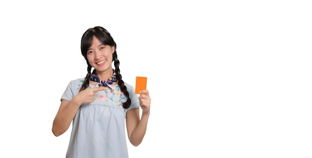 Retrato de uma bela jovem asiática feliz em vestido jeans segurando cartão de crédito em fundo branco