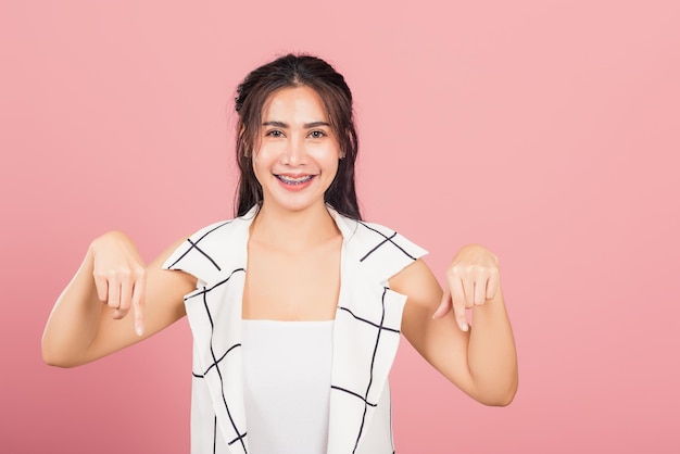 Retrato de uma bela jovem asiática infeliz, gesto negativo mostrando os polegares para baixo ou sinal de antipatia, tiro de estúdio isolado em fundo rosa, rejeição feminina tailandesa ao contrário do espaço de cópia