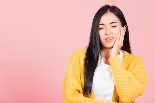 Retrato de uma bela jovem asiática que sofre de dor de dente, problema de dor de dente forte e terrível feminina pressionando a mão no queixo, tiro de estúdio isolado em fundo rosa, conceito de saúde bucal