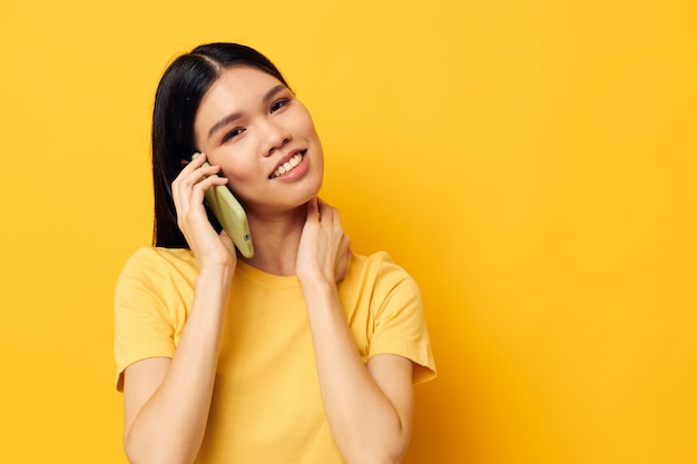 Retrato de uma bela jovem asiática se comunica no telefone emoções fundo amarelo inalterado