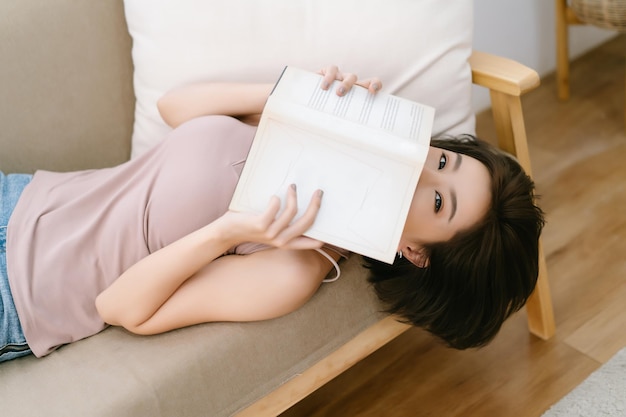 Retrato de uma bela jovem asiática segurando o livro na frente do rosto e olhando para a câmera