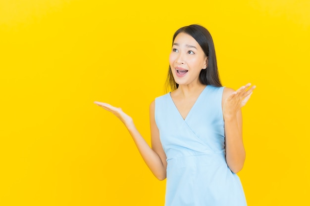 Retrato de uma bela jovem asiática sorrindo com ação na parede de cor amarela