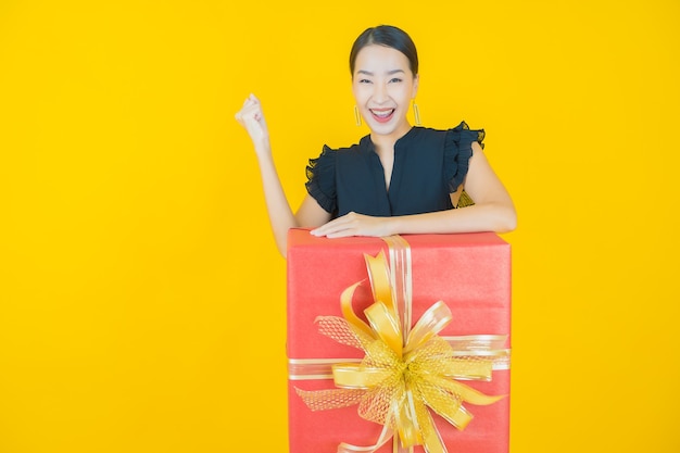 Retrato de uma bela jovem asiática sorrindo com caixa de presente vermelha em amarelo