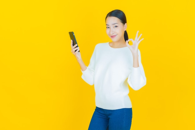 Retrato de uma bela jovem asiática sorrindo com um celular inteligente em amarelo