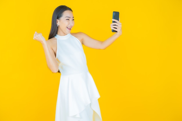 Retrato de uma bela jovem asiática sorrindo com um celular inteligente em amarelo