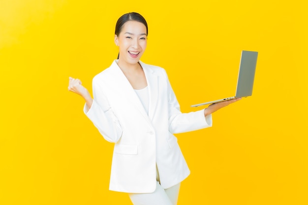 Retrato de uma bela jovem asiática sorrindo com um laptop na parede isolada