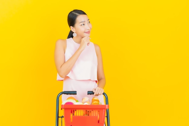 Retrato de uma bela jovem asiática sorrindo com uma cesta de supermercado em amarelo