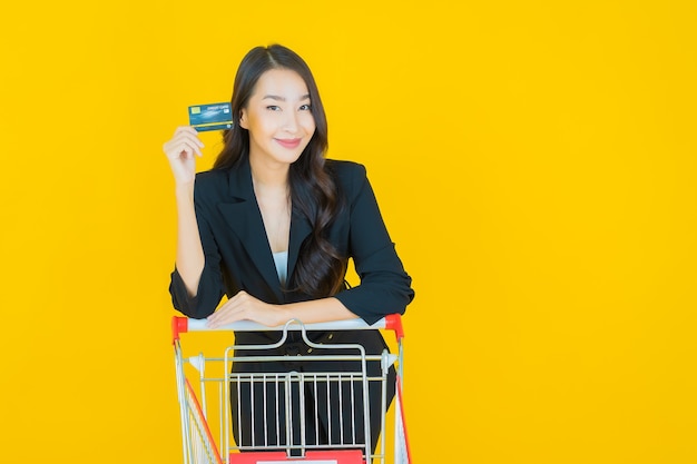 Retrato de uma bela jovem asiática sorrindo com uma cesta de supermercado em amarelo