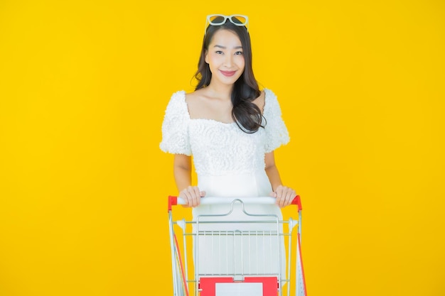 Foto retrato de uma bela jovem asiática sorrindo com uma cesta de supermercado em amarelo