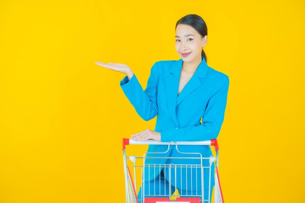 Retrato de uma bela jovem asiática sorrindo com uma cesta de supermercado em amarelo