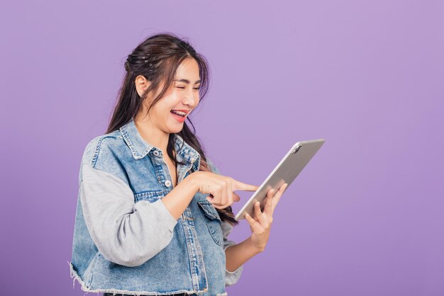 Retrato de uma bela jovem asiática sorrindo usando computador tablet, tela sensível ao toque de uma adolescente feminina de estilo de vida feliz no tablet pc digital, tiro de estúdio isolado em fundo roxo