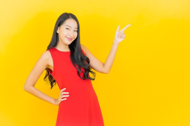 Retrato de uma bela jovem asiática usando um vestido vermelho e sorrindo com ação na parede amarela