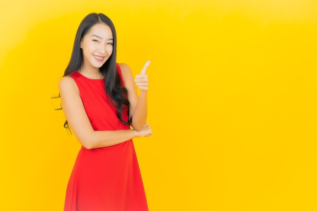 Retrato de uma bela jovem asiática usando um vestido vermelho e sorrindo com ação na parede amarela