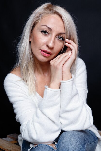 Retrato de uma bela jovem atraente com uma camisola branca com olhos azuis e longos cabelos loiros.