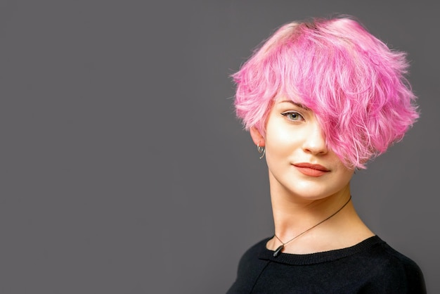 Retrato de uma bela jovem branca com um penteado curto rosa em fundo escuro com espaço de cópia.