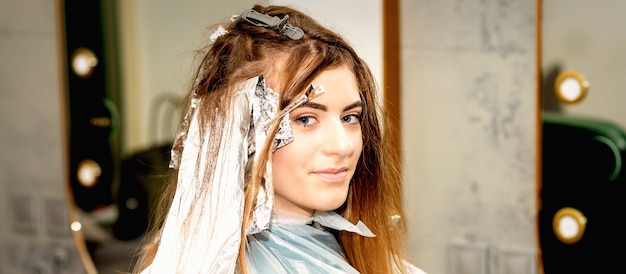 Retrato de uma bela jovem caucasiana, aplicando papel alumínio no cabelo antes de tingir em um salão de beleza