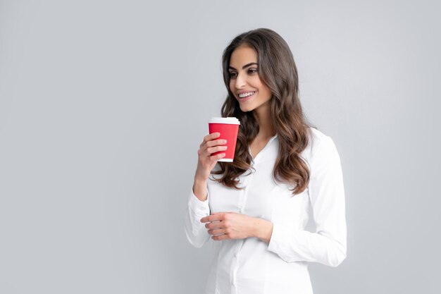 Retrato de uma bela jovem com uma xícara de café em pé sobre o fundo cinza