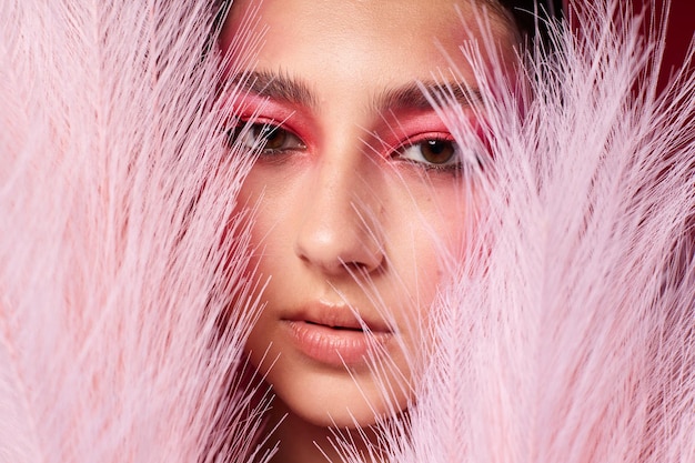 Retrato de uma bela jovem de penas cor-de-rosa maquiagem de rosto rosa posando um olhar atraente fundo rosa inalterado