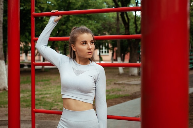 Retrato de uma bela jovem desportista. Fitness, treino, ao ar livre. Corpo musculoso treinado. Parque, campo de esportes. Um estilo de vida saudável.