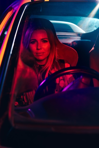 Retrato de uma bela jovem dirigindo o carro à noite na luz neon