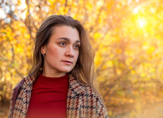 Retrato de uma bela jovem em um parque de outono ao sol