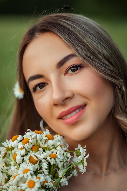 Retrato de uma bela jovem em um vestido branco com uma camomila em suas mãos caminhada de verão nas montanhas