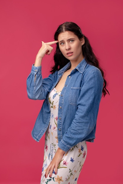 Retrato de uma bela jovem em um vestido leve e camisa azul em pé sobre fundo rosa em parafuso prisioneiro.