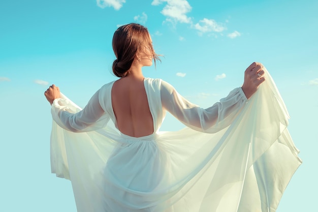 Foto retrato de uma bela jovem em um vestido longo branco contra o céu. vestido ao vento