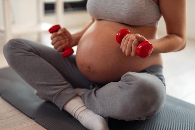 Foto retrato de uma bela jovem grávida sentada perto de um exercício. usando pesos.