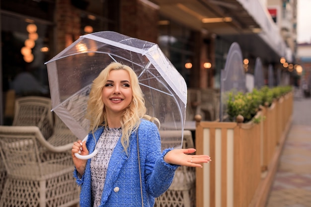 Retrato de uma bela jovem loira segurando um guarda-chuva transparente na chuva em uma rua da cidade