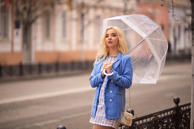 Retrato de uma bela jovem loira segurando um guarda-chuva transparente na chuva em uma rua da cidade