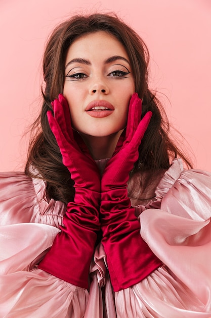 Retrato de uma bela jovem morena com maquiagem brilhante e roupas da moda em pé isolado na parede rosa, posando