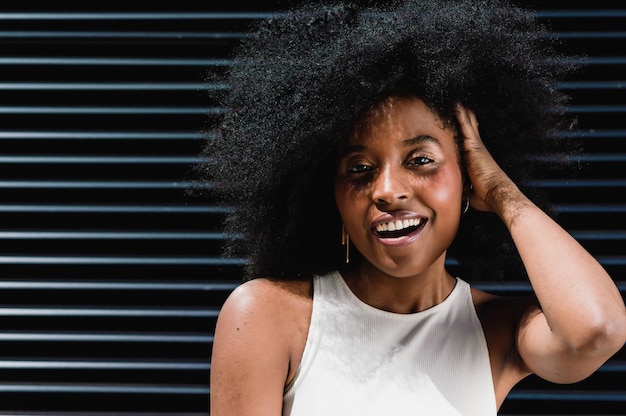 Retrato de uma bela jovem morena latina hispânica com afro, ao ar livre, com a mão na cabeça, muito feliz sorrindo e olhando para a câmera com travessura e cumplicidade. conceito de estilo de vida.