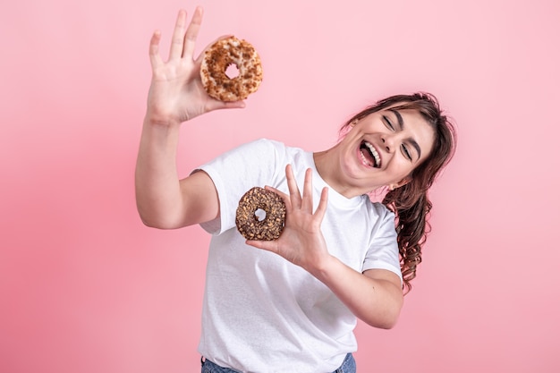 Retrato de uma bela jovem mostrando rosquinhas isoladas sobre fundo rosa