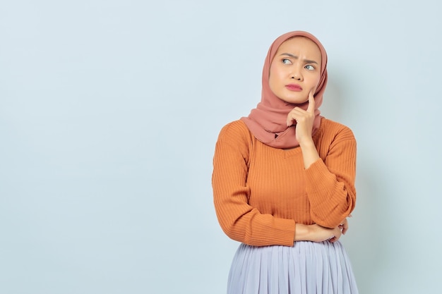 Retrato de uma bela jovem muçulmana asiática de suéter marrom olhando sério pensando em questão e olhando para o espaço de cópia isolado no fundo branco conceito de estilo de vida muçulmano